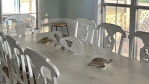 A dining area with a white table, white chairs, a hanging light fixture, and a framed artwork on the wall. - Coastal cottage minutes from the beach.  Large front porch for morning sun!! (Myrtle Beach)