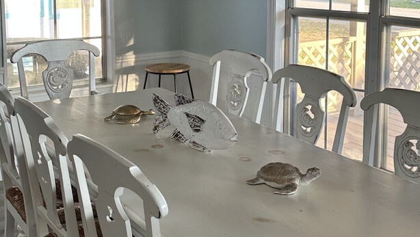 A dining area with a white table, white chairs, a hanging light fixture, and a framed artwork on the wall.