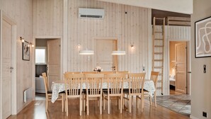 A dining area with a wooden table and chairs, pendant lights, and a view into another room.