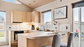 A modern kitchen with wooden cabinets, a central island, and a dining area with two grey chairs.