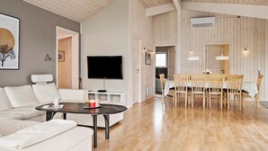 A spacious living room with a flat-screen TV, a dining area with wooden chairs and a table, and a large window providing natural light.