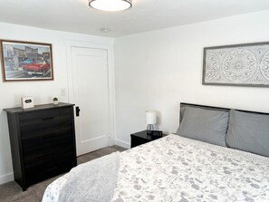 A bedroom with a bed, a dresser, a nightstand, a lamp, and two wall decorations.
