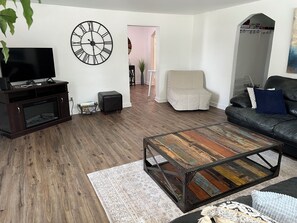 A living room with a television, a clock, a sofa, a coffee table, and a chair.