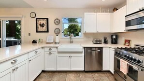 A modern kitchen with white cabinets, a stainless steel dishwasher, a gas stove, and a window with a view of greenery.