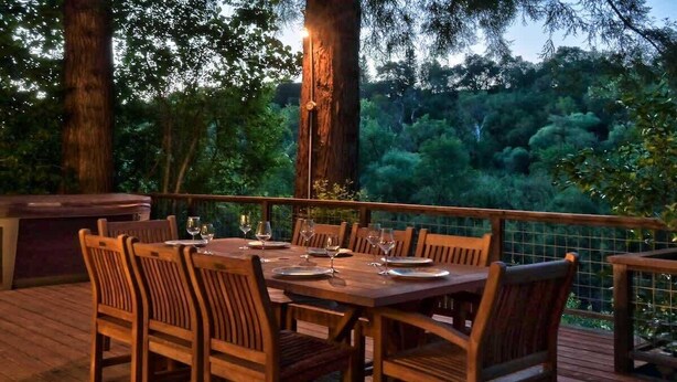 A wooden deck with a table set for dining, surrounded by chairs.