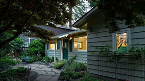 A house with a stone pathway leading to the front door, surrounded by lush greenery and a small garden.