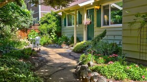 A garden pathway leading to a house with a porch, surrounded by various plants and flowers.