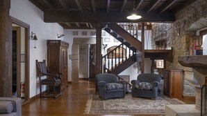 A spacious living room with a wooden staircase, two armchairs, a fireplace, and a stone wall.