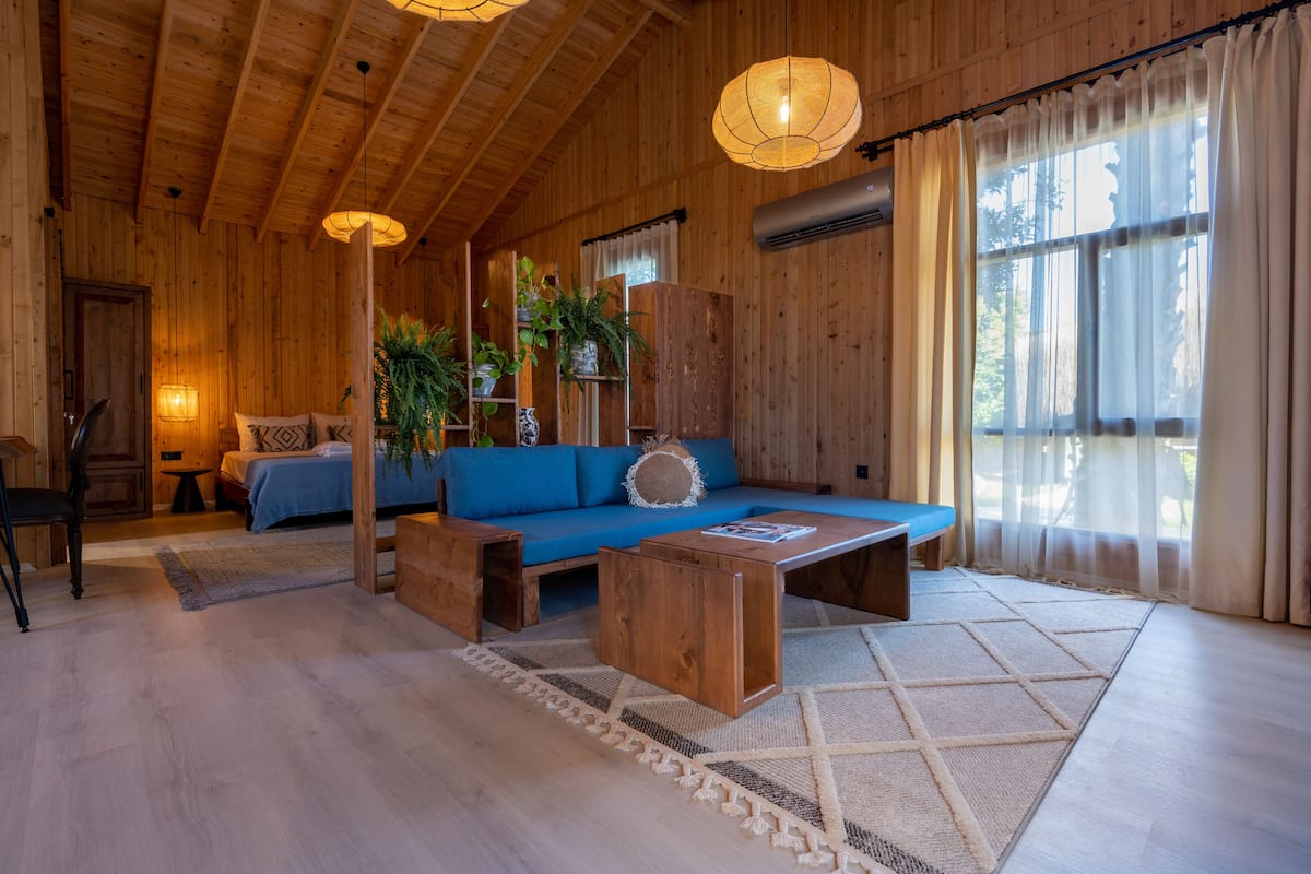 Un interior de madera con un sofá azul, una mesa de centro de madera y un ventanal con cortinas.