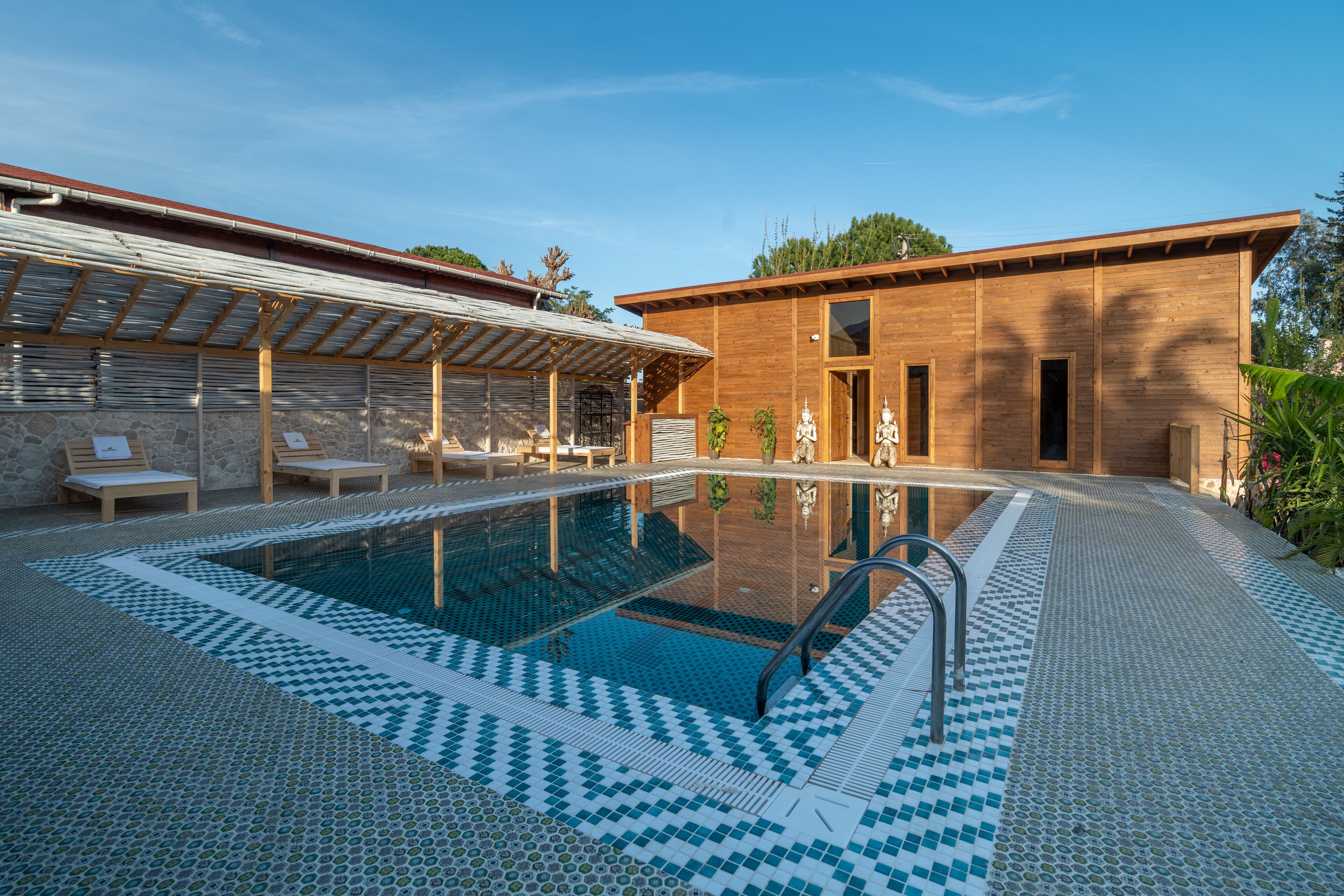 A modern outdoor pool area with a clear blue pool, lounge chairs, and a covered seating area.