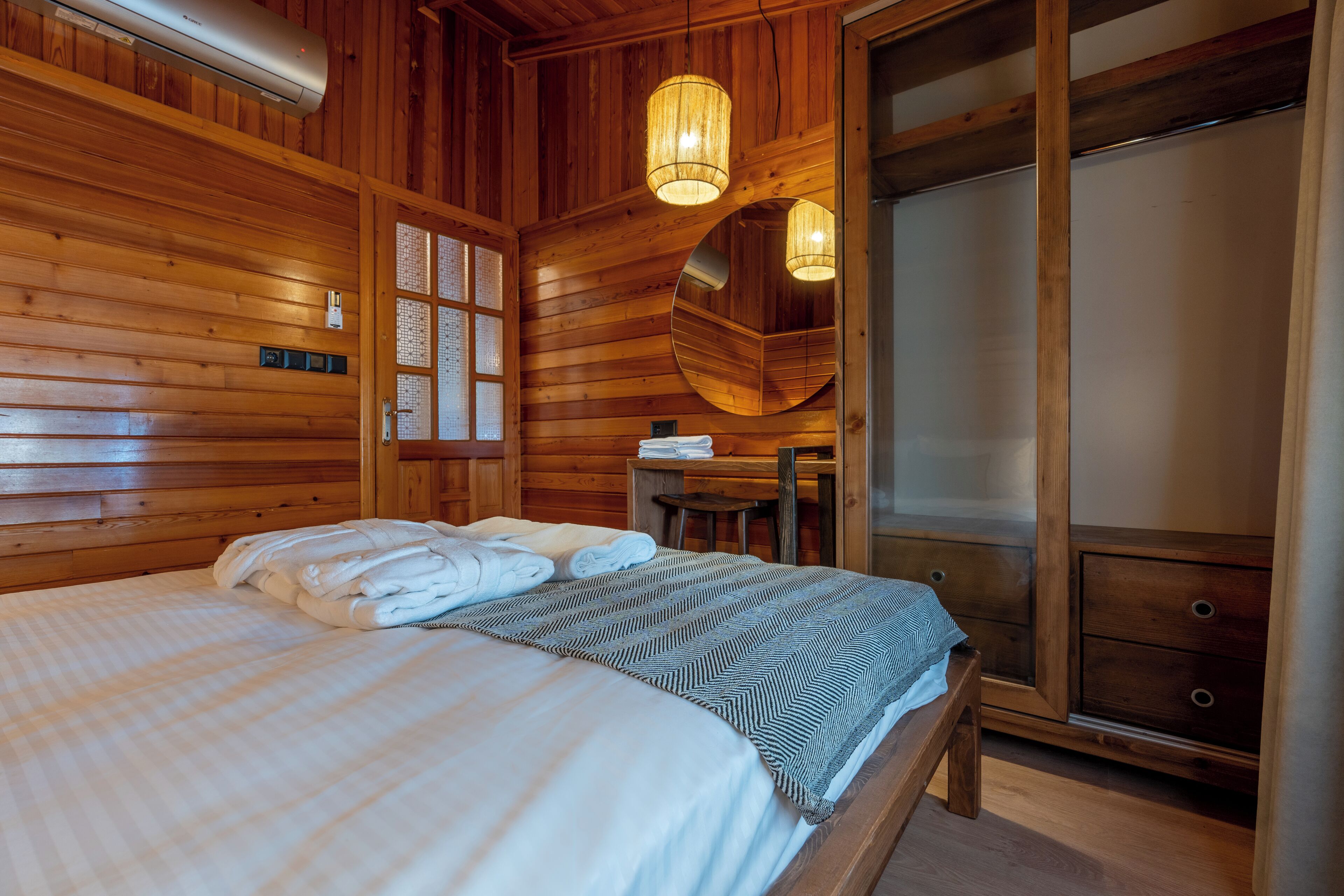 A wooden-paneled bedroom with a bed, a desk, and a mirror.