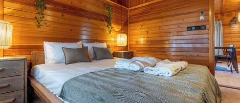 Un dormitorio con paneles de madera, una cama, mesitas de noche y una planta colgante.