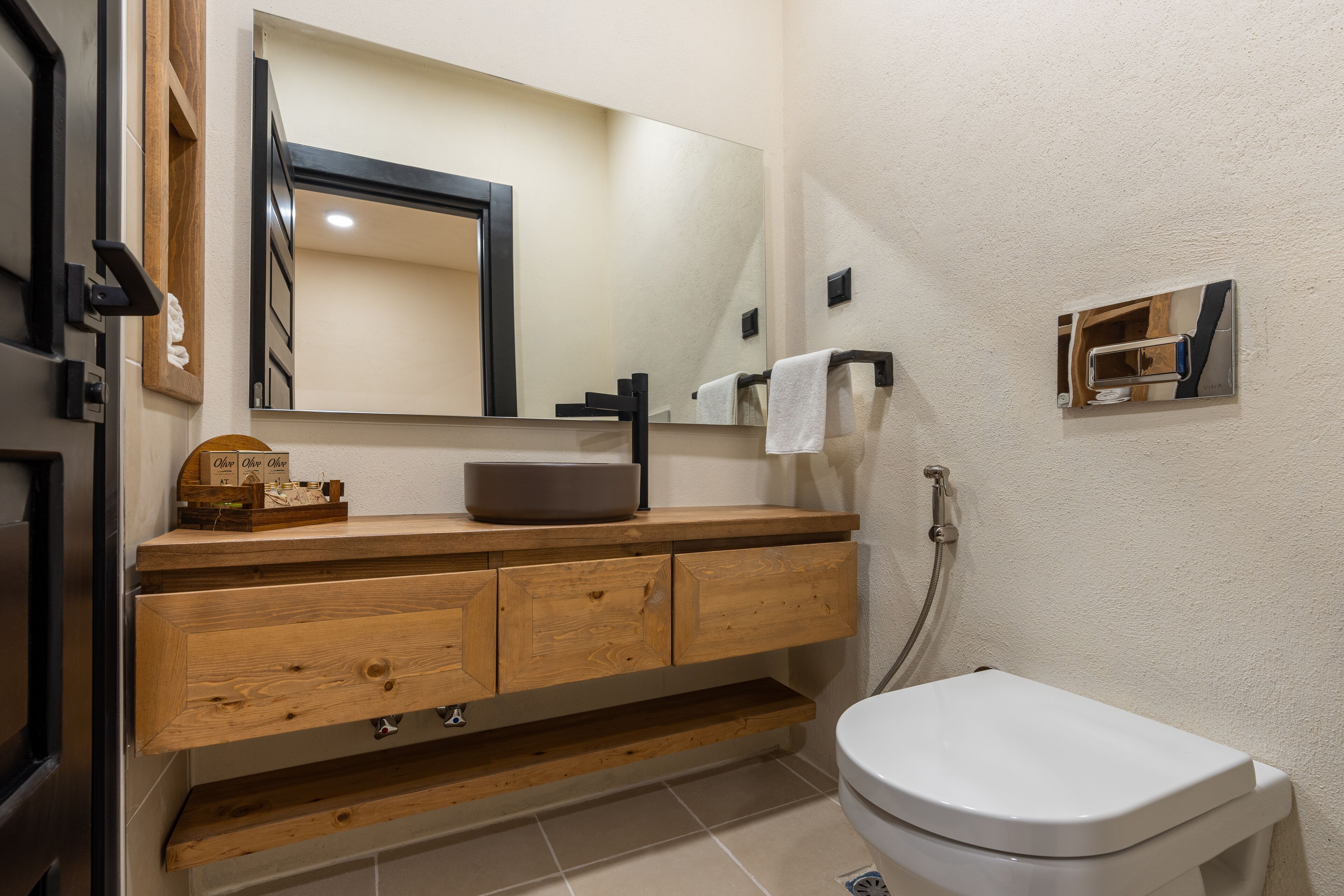 Un baño moderno con tocador de madera, un espejo grande, inodoro blanco y perchero.