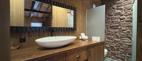 A bathroom with a wooden vanity, a large mirror, a stone wall, and a white sink.