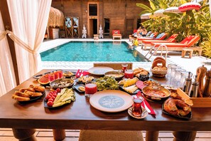 A dining table with a variety of foods and drinks, a pool in the background, and lounge chairs. - Naturelife Bungalows & SPA - Free Access to Odile Hotel (Kemer)