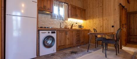 A wooden interior with a kitchen area, including a refrigerator, washing machine, and dining table with chairs.