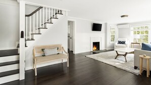 A spacious living room with a dark wood floor, a white staircase, a fireplace, a sofa, and a television mounted on the wall.