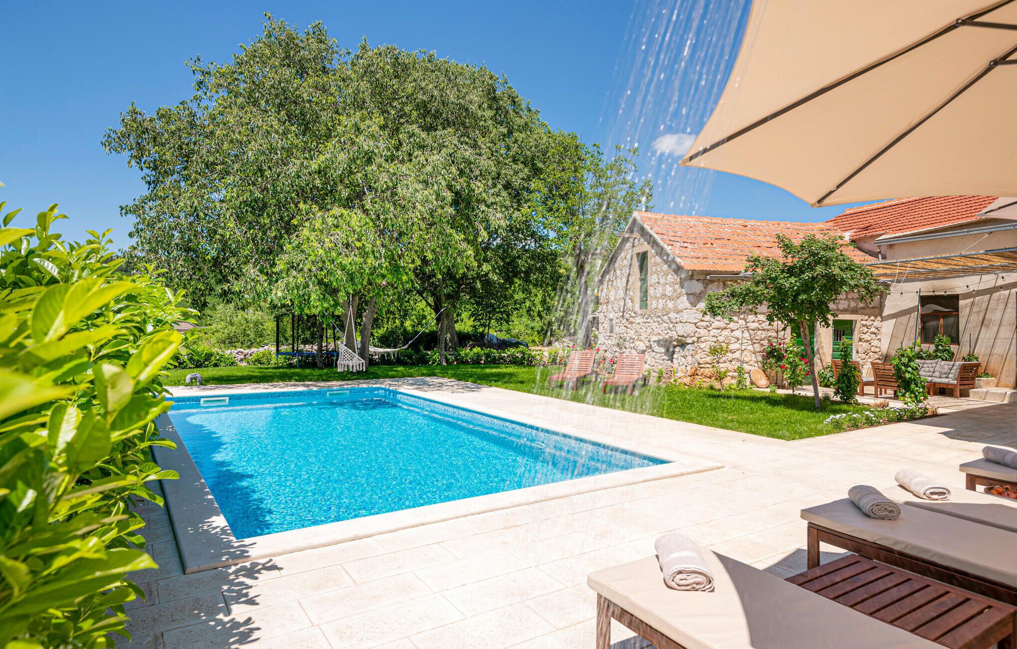 Una piscina con una casa de piedra al fondo, rodeada de vegetación.