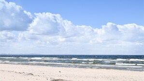 Ein Strand mit Wellen, blauem Himmel und weiter Küste.