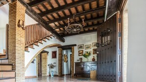 Un passadís ample amb una escala de fusta, una gran porta de fusta i un penjall.