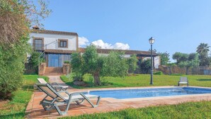 Zona de piscina amb gandules, un camí de pedra i una casa amb teulada de teules.