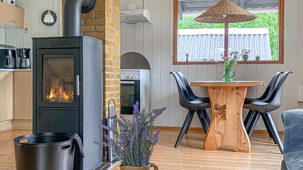 Een keuken met een houtkachel, een eettafel met stoelen en een raam met uitzicht op groen.