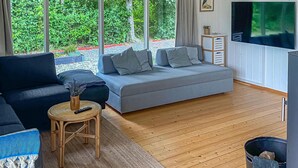 Een moderne woonkamer met een grijze bank, een donkerblauwe bank, een klein houten tafeltje met een afstandsbediening, en een televisie aan de muur.