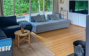 Ein modernes Wohnzimmer mit einem grauen Sofa, einem dunkelblauen Couch und einem kleinen Holztisch mit einer Fernbedienung. An der Wand ist ein Fernseher angebracht.