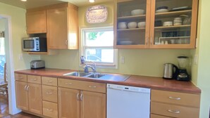 A kitchen with wooden cabinets, a dishwasher, a microwave, a toaster, a sink, and a window with a view of the outside. - Charming, light-filled SE Eugene 2-story house  (Eugene)