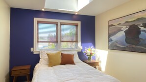 A bedroom with a skylight, a bed with white bedding, a nightstand, a window with blinds, and a painting on the wall. - Charming, light-filled SE Eugene 2-story house  (Eugene)