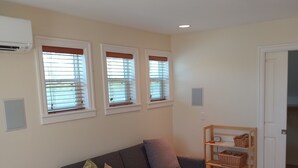 A living room with a grey sofa, three windows with blinds, a ceiling light fixture, a wooden floor, and a patterned rug. - Charming, light-filled SE Eugene 2-story house  (Eugene)