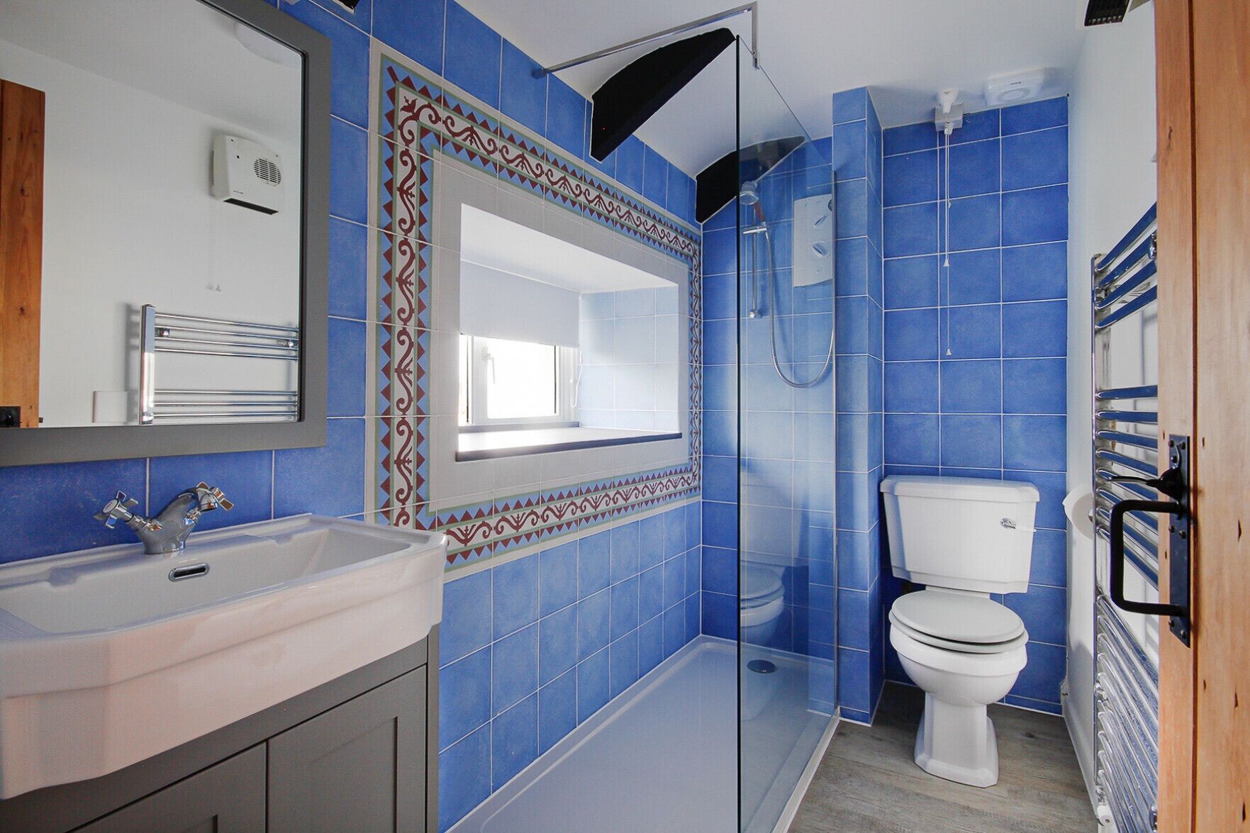 A bathroom with blue tiles, a white sink, a mirror, and a toilet.