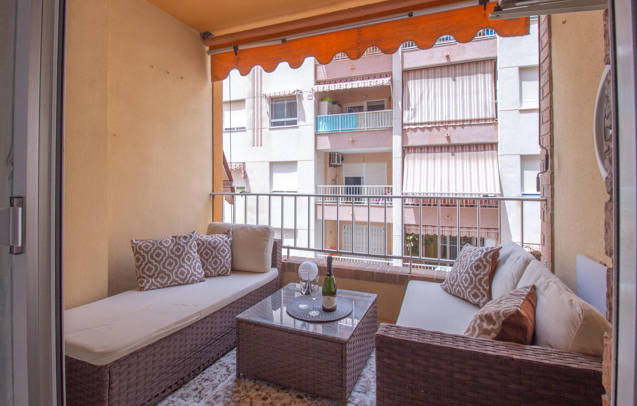 A balcony with wicker furniture, a glass table, and a bottle of wine.