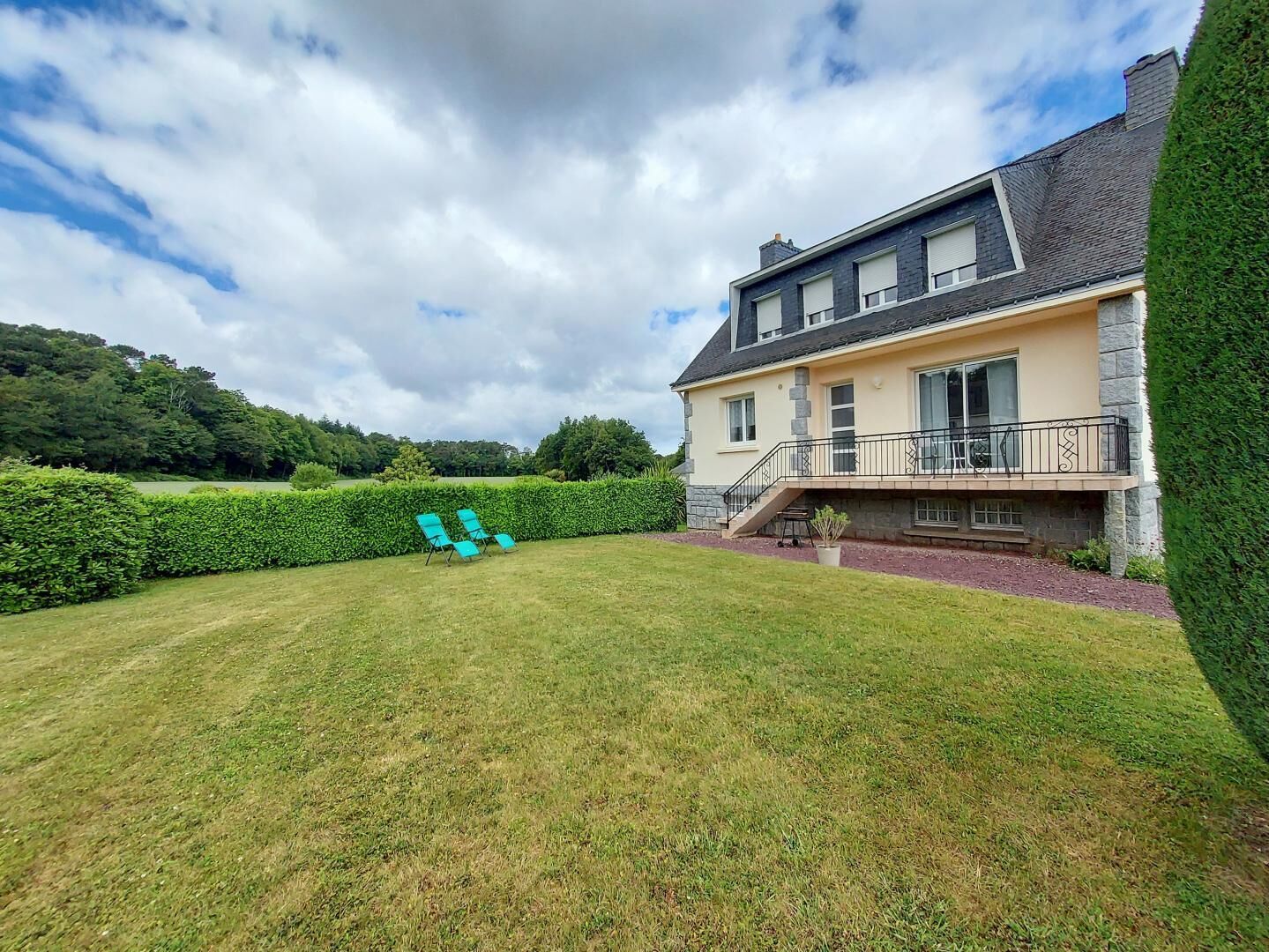 A house with a large backyard, a balcony, and a staircase leading to the entrance.