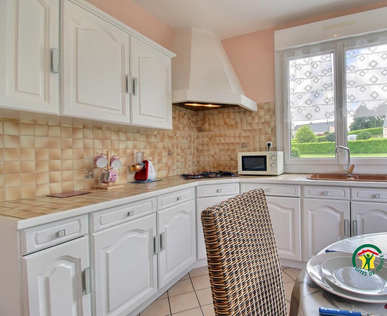A kitchen with white cabinets, a microwave, a stove, and a window with a view of greenery.