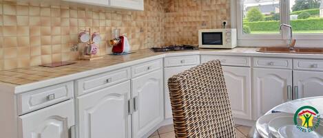 A kitchen with white cabinets, a microwave, a stove, and a window with a view of greenery.