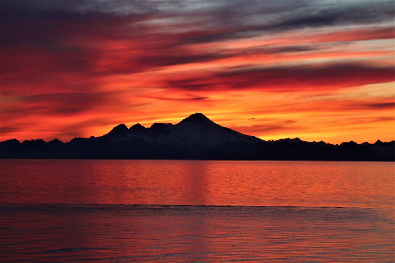 A mountain silhouette at sunset with a calm body of water in the foreground.