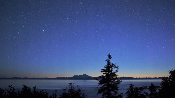 A night sky filled with stars over a calm body of water with mountains in the distance. - Ocean-view Cabins on the Anchor Point Bluff (Anchor Point)