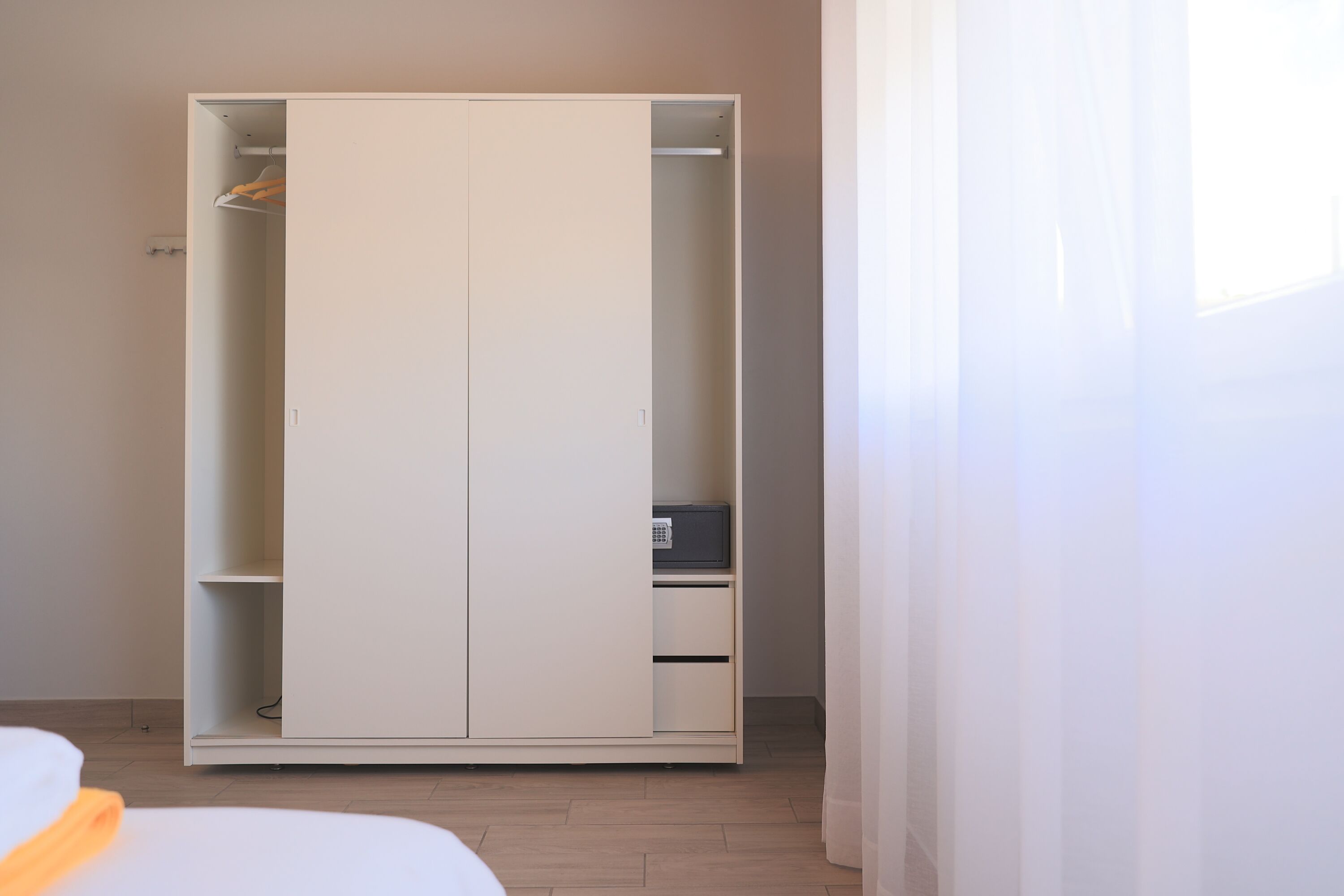 Une chambre dotée d’une grande armoire, d’un lit et d’une fenêtre ornée de rideaux légers.