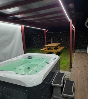 Ein Whirlpool mit Holztisch und Bänken in einem überdachten Außenbereich.