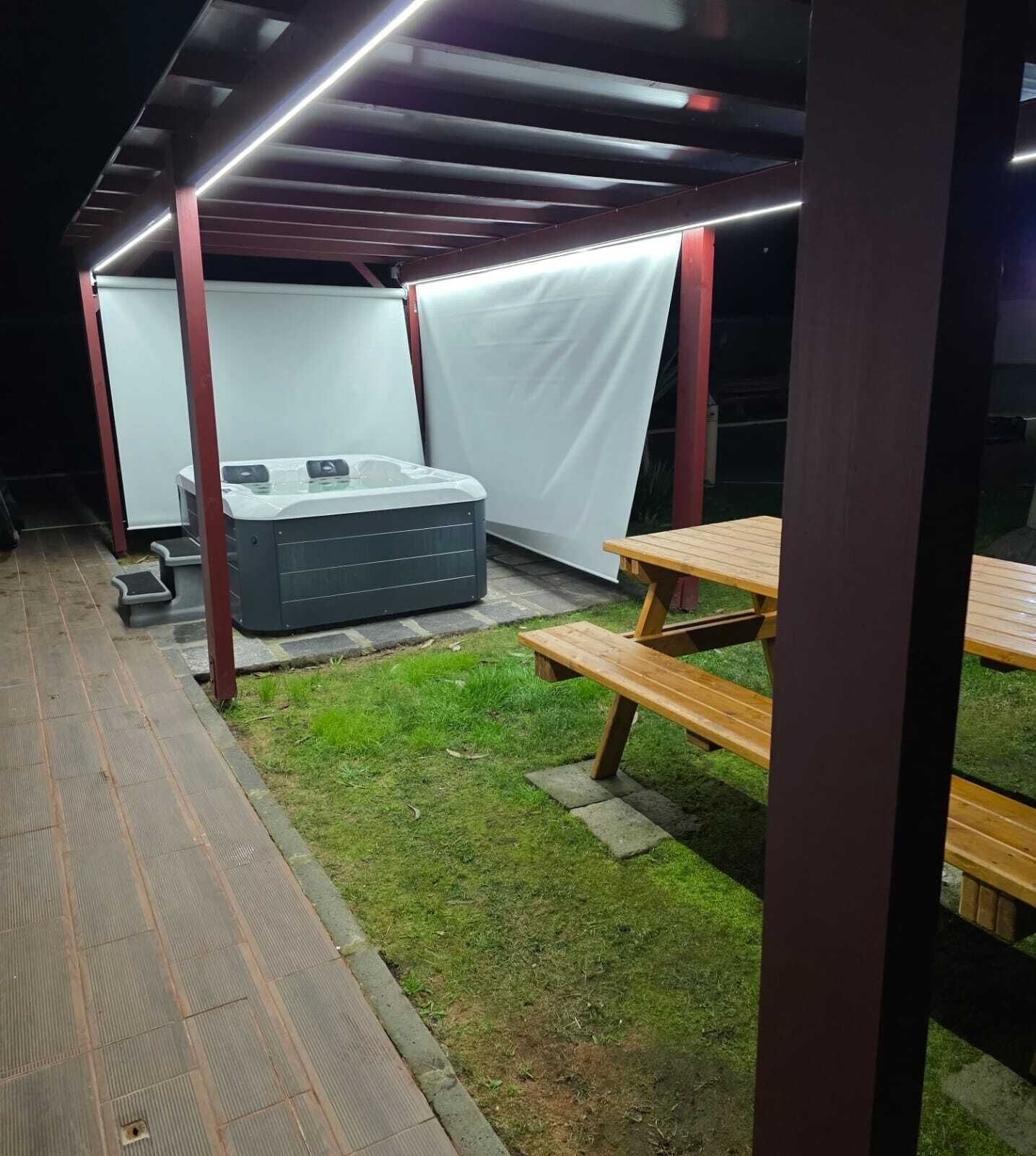 Un espace extérieur abrité comprenant un jacuzzi, une table de pique-nique et des marches menant à une entrée couverte.