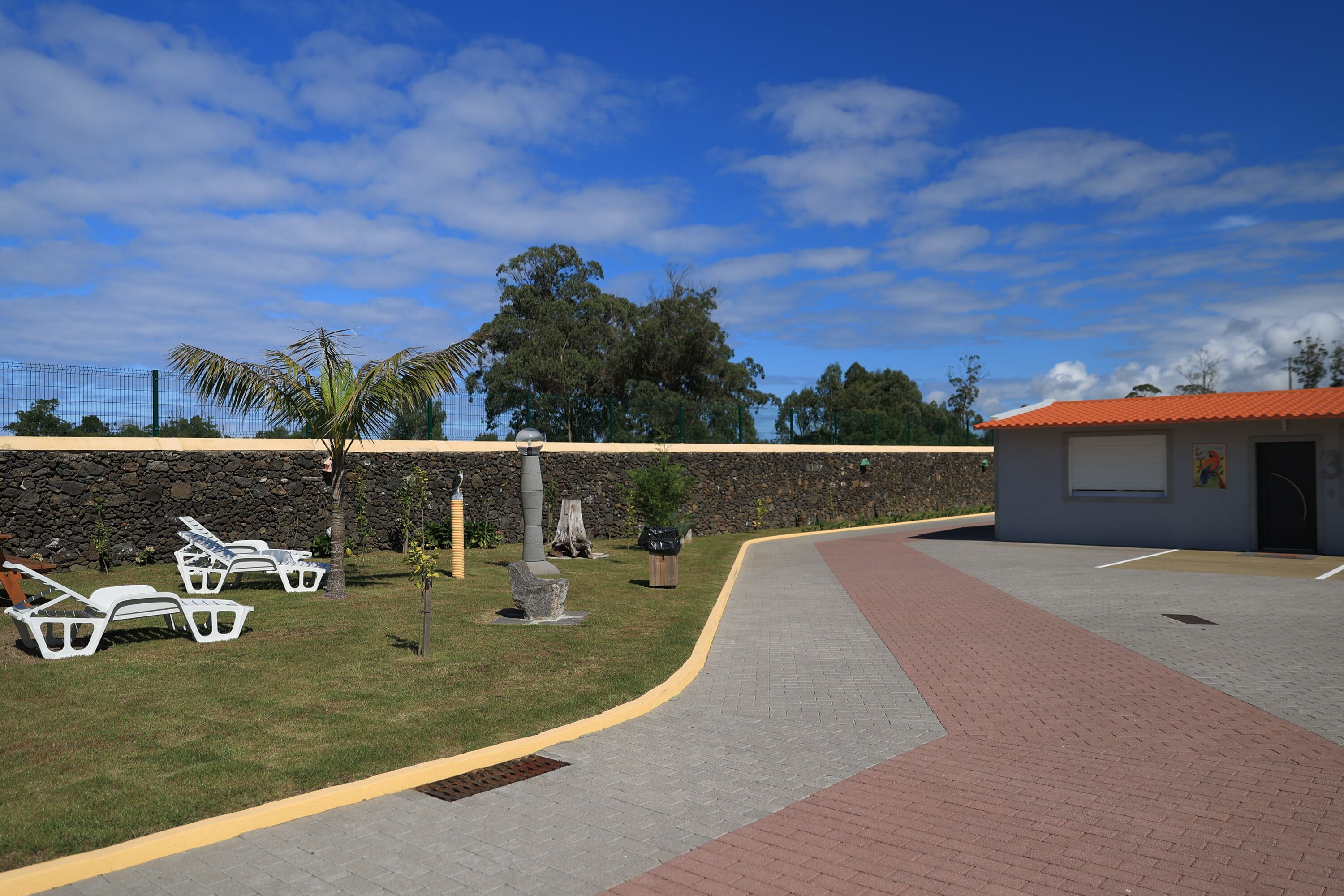 A paved walkway with a curved path, a stone wall, and a building with a red roof.