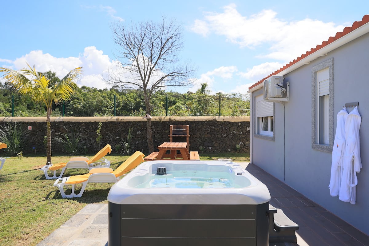 A hot tub with lounge chairs, a stone wall, and a wooden deck.