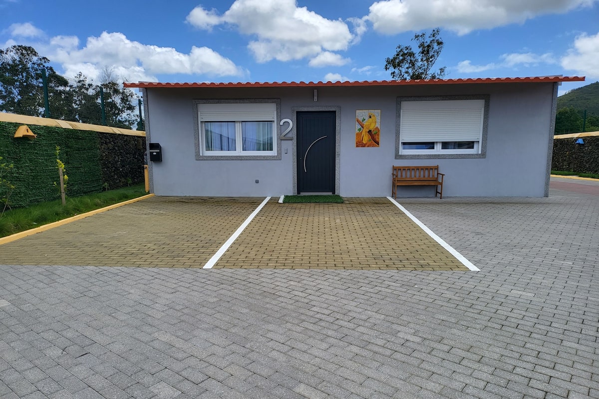 A small building with a red roof, a black door, and a window with a white blind. There is a bench to the right of the door and a yellow object on the left.