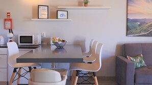 A modern dining area with a table, chairs, a microwave, a basket of fruits, and a painting on the wall. - Parrots Village (Ribeira Grande)
