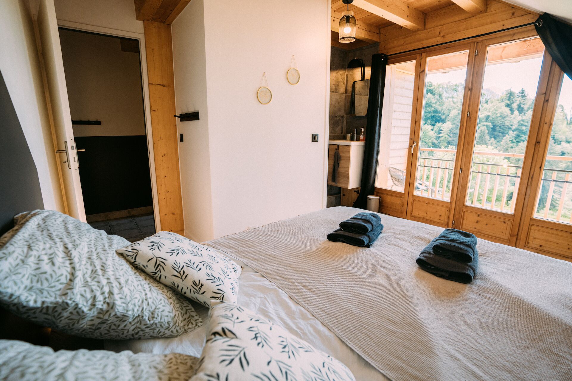 A bedroom with a bed, pillows, a wooden ceiling, a window with a view of trees, and a small shelf with items.