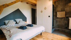 A bedroom with a bed, wooden beams, a stone wall, and a towel hanging on the wall. - CHALET DE LA FOUGERE 15 PERS 180M2 BAUGES (Thoiry)