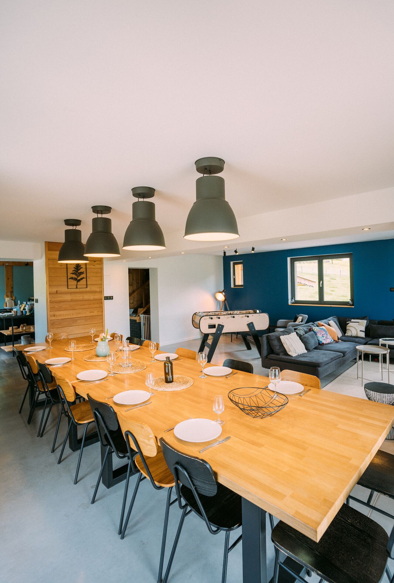 A modern dining area with a long wooden table set for six, black chairs, and pendant lighting.