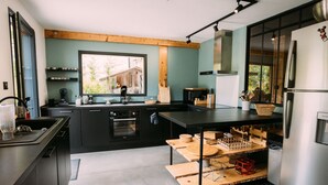A modern kitchen with a large window, built-in appliances, and a wooden island. - CHALET DE LA FOUGERE 15 PERS 180M2 BAUGES (Thoiry)