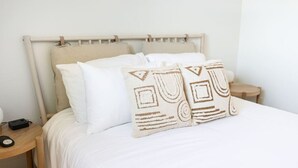 Een bed met witte lakens en twee decoratieve kussens met geometrische patronen.